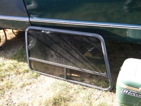 1981 Ford E350 - A detached window from a van sits on the ground beside the vehicle it was removed from.