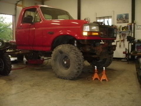 1995 Ford F-150 - This red 1995 Ford F-150 is shown in a garage, lifted on jack stands with oversized tires.