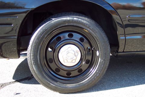 2001 Ford Crown Victoria - Close-up of a black steel wheel with a chrome hubcap on a dark-colored vehicle.