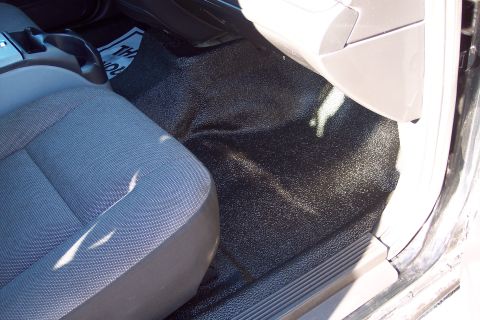 2001 Ford Crown Victoria - The interior of a vehicle shows a textured black floor and the driver's seat, with some readable text on a mat partially visible.