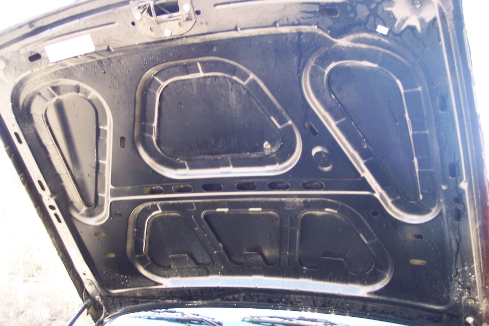 Underside of a dark-colored car hood, showing insulation and structural supports