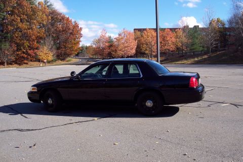 2001 Ford Crown Victoria - A black police car is parked in a lot with autumn foliage visible in the background.