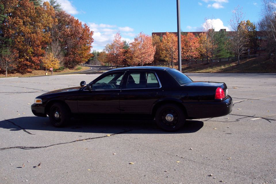 Black police car parked in a lot, side view. Autumn trees in background