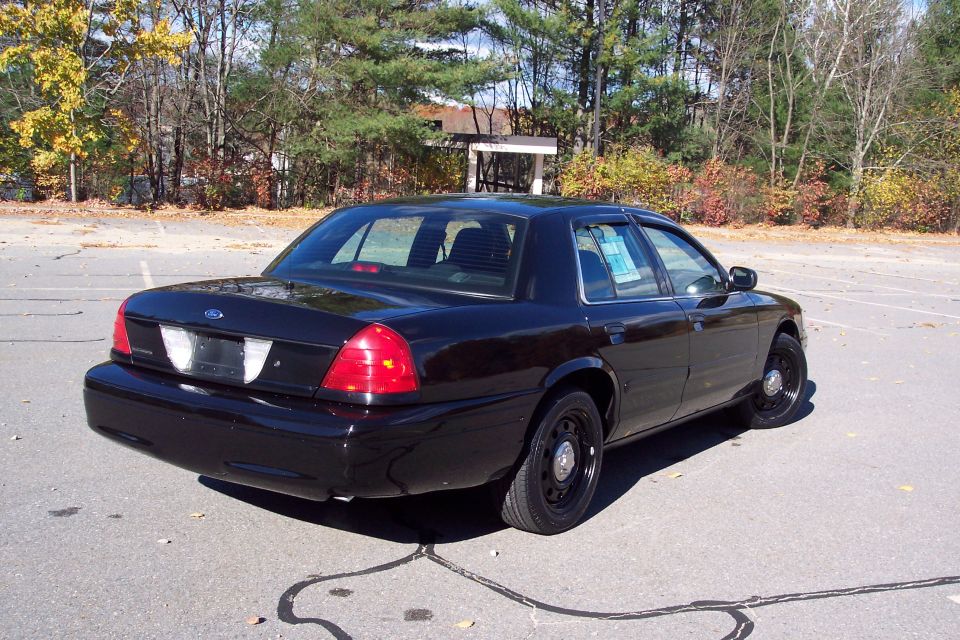 Black Ford Crown Victoria parked on asphalt with trees in background