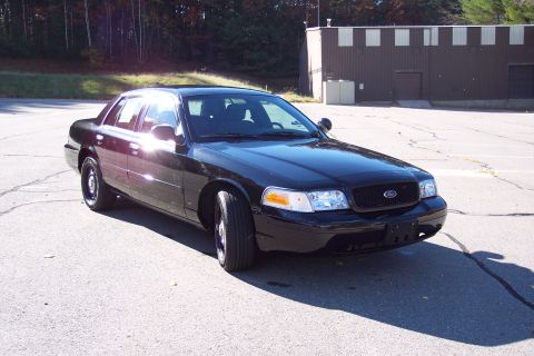2001 Ford Crown Victoria - A black 2001 Ford Crown Victoria Police Interceptor is parked in an asphalt lot with a building in the background.