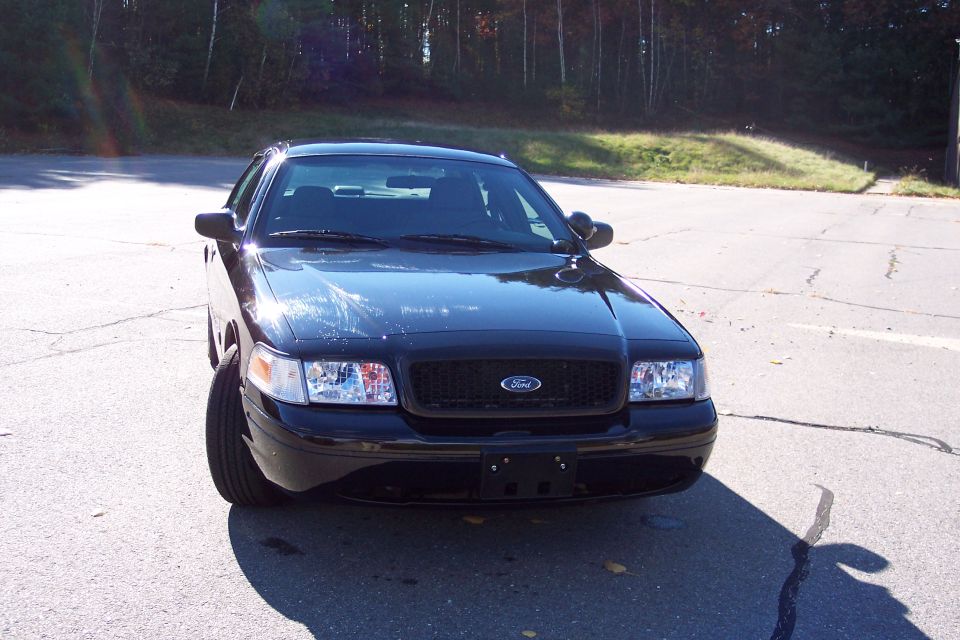 Black Ford Crown Victoria parked on asphalt, front view. Grille and headlights are visible
