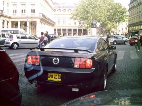 1991 Ford Crown Victoria - A black Ford Mustang is seen from the rear on a city street with other vehicles and pedestrians.
