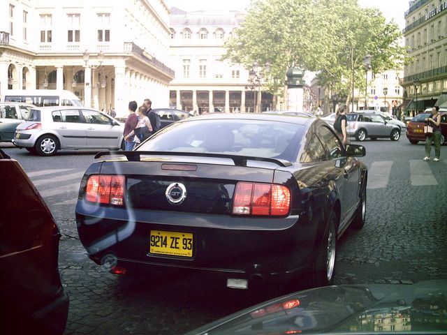 Black Ford Mustang parked on a city street, rear view. Yellow license plate reads 9214 ZE 93