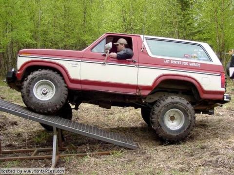 1985 Ford Bronco - A red and white 1985 Ford Bronco is shown on a ramp, likely participating in an off-road event.
