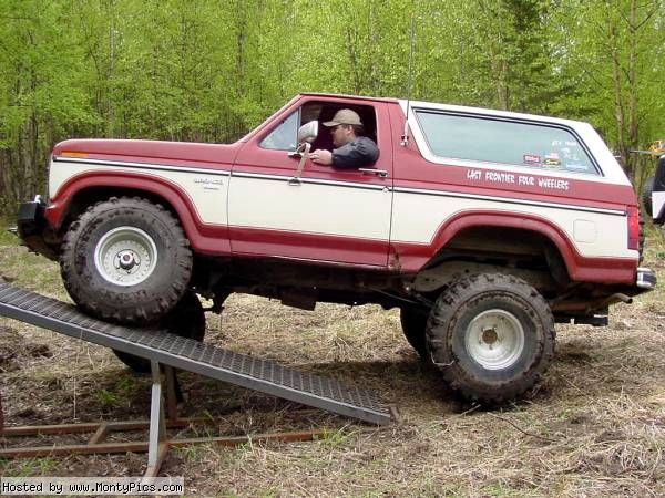 Red and white lifted Ford Bronco on off-road ramp with driver in cowboy hat