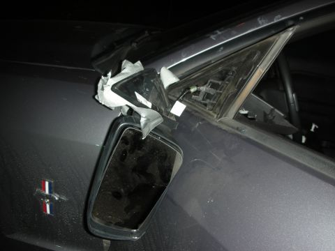 1998 Ford Crown Victoria - Side mirror assembly is damaged and partially covered with tape on a dark gray car.