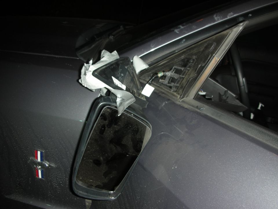 Dark gray car fender with a damaged side mirror assembly and a Ford Mustang emblem