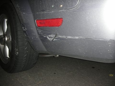 1998 Ford Crown Victoria - Damage to the rear bumper of a gray car is visible, including a significant scratch and scuff marks.