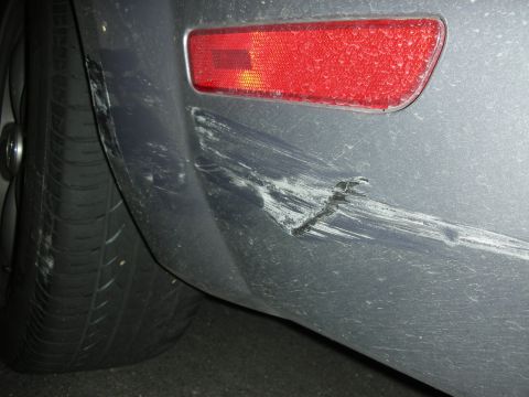 1998 Ford Crown Victoria - Scratches and a gouge mar the rear bumper of a gray vehicle, located near the red taillight.