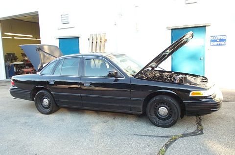 2001 Ford Crown Victoria - A black 2001 Ford Crown Victoria is parked outside a building with its hood open, revealing the engine compartment.