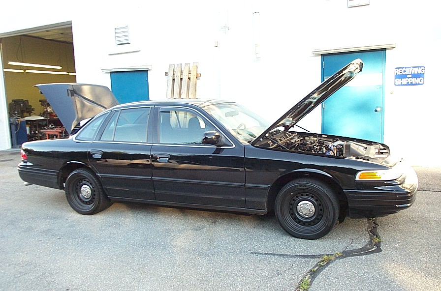 Black 2001 Ford Crown Victoria with hood open, parked outside a building with a 'Receiving Shipping' sign