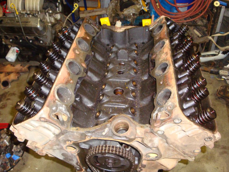 Engine block with valve springs and timing chain visible, in a workshop setting