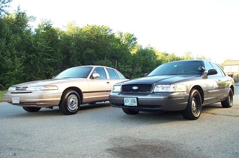 2001 Ford Crown Victoria - Two Ford Crown Victorias, a tan model and a dark gray model, are parked side-by-side.