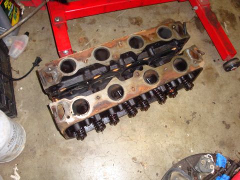 1989 Ford Bronco - Two V8 engine cylinder heads sit on the floor, ready for cleaning or repair.
