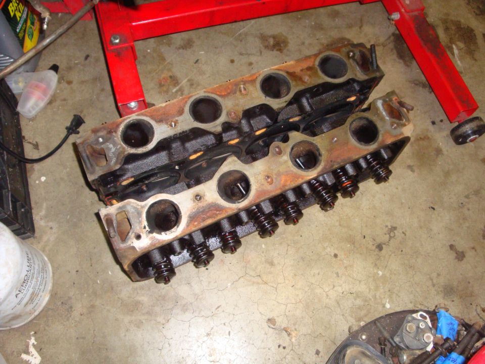 pair of V8 engine cylinder heads on concrete floor, red engine stand in background