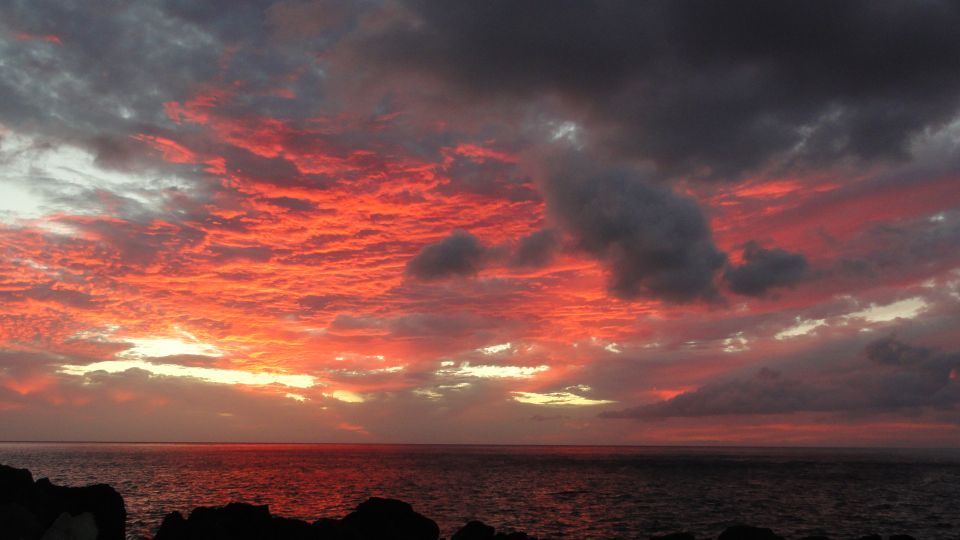 Red sunset over ocean with dark clouds and rocky shoreline silhouette