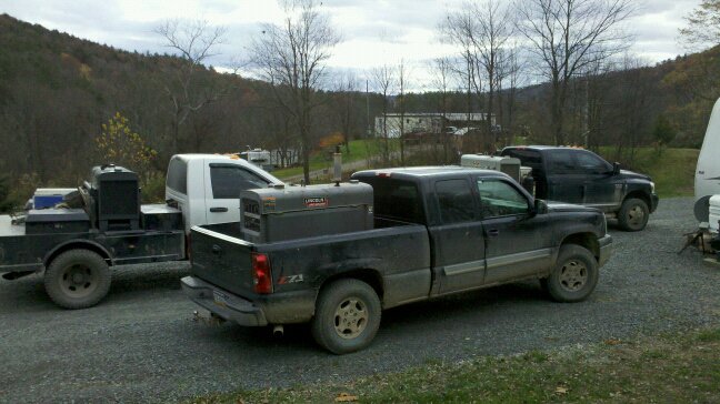 Black Chevy Silverado pickup with bed-mounted welder and toolboxes on a gravel lot
