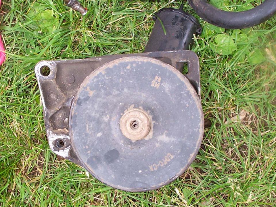 Used power steering pump with black pulley and mounting bracket lying in grass, marked E0TC-CA