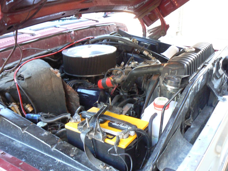 1978 Ford Bronco engine bay with a large air filter, yellow battery, and red hoses