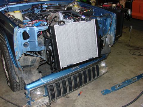 1991 Jeep Comanche - The front end of a blue Jeep Comanche is disassembled, showing the engine bay and radiator area during a repair process.