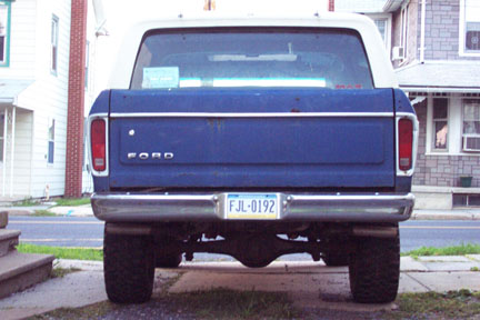 1979 Ford Bronco - This blue Ford Bronco is parked in front of a residential building, showing its rear end and license plate.