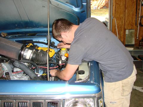 1991 Jeep Comanche - A man works on the engine of a blue 1991 Jeep Comanche.