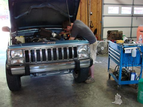 1991 Jeep Comanche - A man works on the engine of a blue Jeep Comanche pickup truck in a garage, with a toolbox nearby.