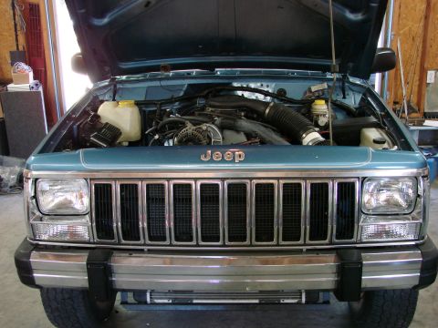 1991 Jeep Comanche - The engine bay of a Jeep Cherokee is visible with the hood raised, the grille and front-end details.