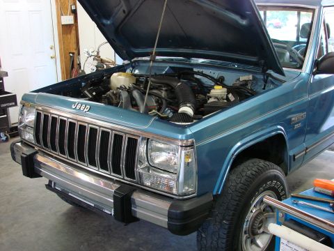 1991 Jeep Comanche - A blue 1991 Jeep Comanche is shown with its hood open, revealing the engine compartment and front grille.