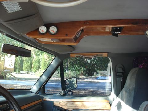 1992 Ford C-350 (Centurion Conversions) - Interior view of a truck cab showing a custom wood-grain overhead console with two round aftermarket gauges and a light, plus a wood-trimme…