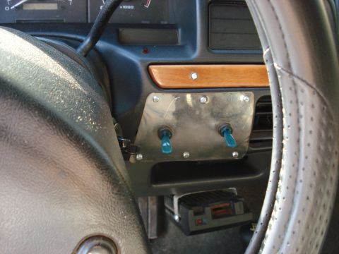 1992 Ford C-350 (Centurion Conversions) - Interior detail of a 1990s Ford truck dash showing a homemade polished-metal panel with two blue-tipped toggle switches screwed in beside t…