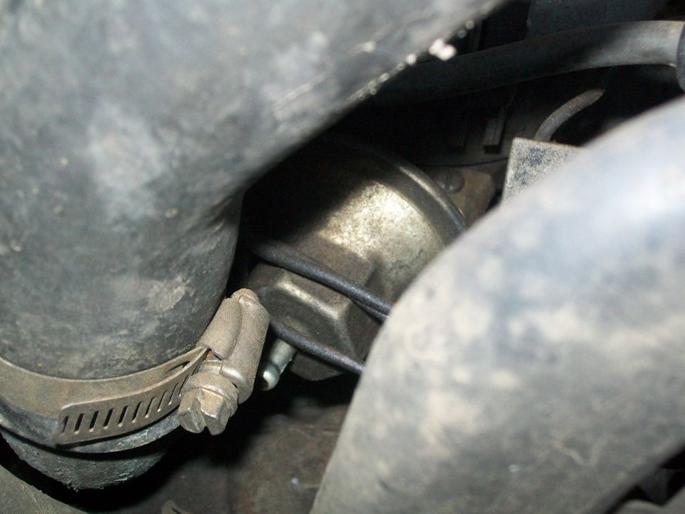 Close-up of a metal engine component with a hose clamp and rubber hoses