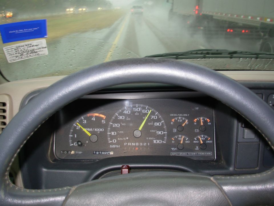 Truck gauge cluster with tach and speedo shot through windshield in the rain on a highway