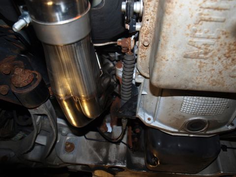 1998 Ford Crown Victoria - Under-car close-up of a stainless header collector merging into a polished exhaust pipe, the tubing burnished gold from heat, tucked alongs…