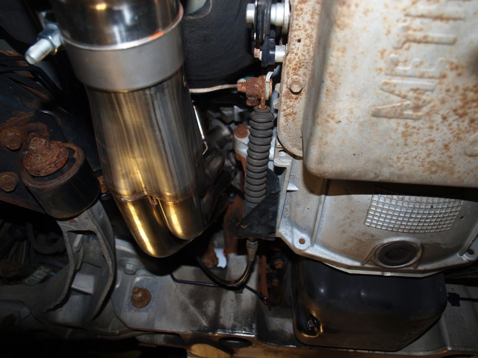 Gold heat-tinted stainless header collector beside aluminum oil pan under car