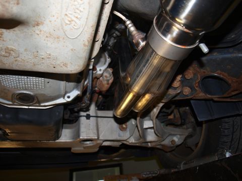 1998 Ford Crown Victoria - Close-up from underneath showing the merge collector of a stainless header joined by a band clamp to a polished exhaust pipe, the metal hea…