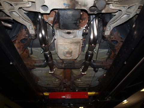 1998 Ford Crown Victoria - Underbody shot from beneath a car on a shop lift, looking rearward along a pair of polished stainless dual exhaust pipes running past the a…