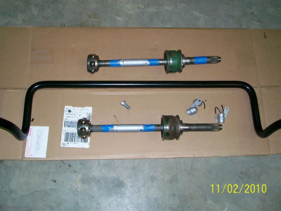 Two driveshafts with blue tape and green components, and a black sway bar on a cardboard surface