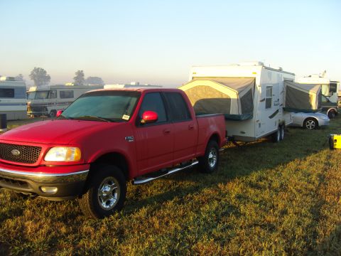 2007 Ford Mustang - A red Ford F-150 pickup truck is seen from the side, towing a pop-up camper trailer in a field.