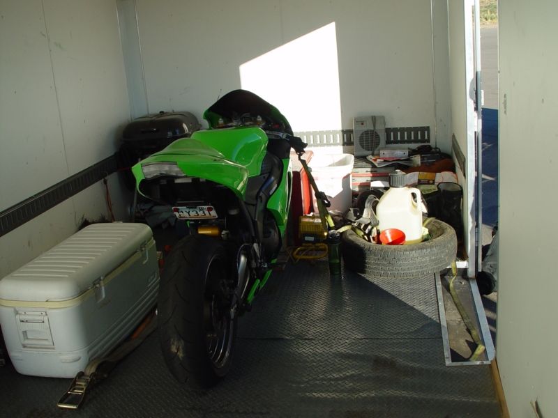 Green Kawasaki Ninja R motorcycle parked in a trailer with a cooler and spare tire