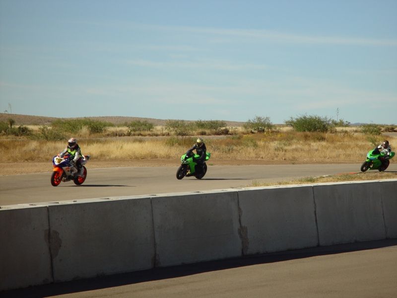 Three motorcycles racing on a track, one orange and white, two green