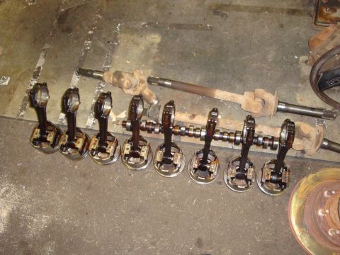 1989 Ford Bronco - Engine parts, including pistons, connecting rods, crankshaft, and driveshafts, are laid out on a concrete floor.