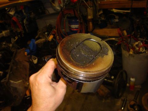 1989 Ford Bronco - A hand holds a used engine piston, showing significant carbon deposits on its crown.