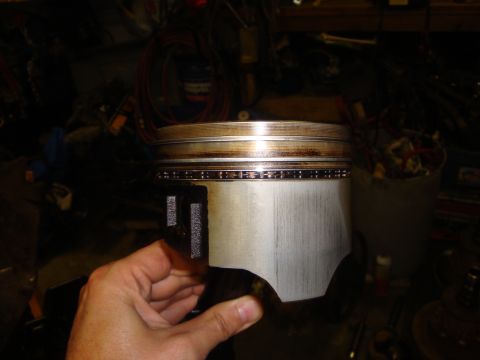1989 Ford Bronco - A piston with its rings is held up for inspection in a cluttered workshop environment.