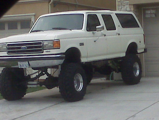 Lifted white SUV with large tires, front grille visible